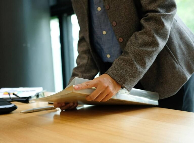 Une personne vêtue d'un blazer gris remettant un dossier sur une table en bois dans un bureau.